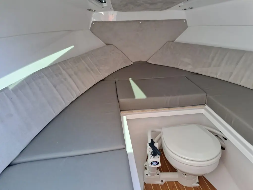 Interior view of a boat cabin featuring grey upholstered seating and a marine toilet positioned at the corner.